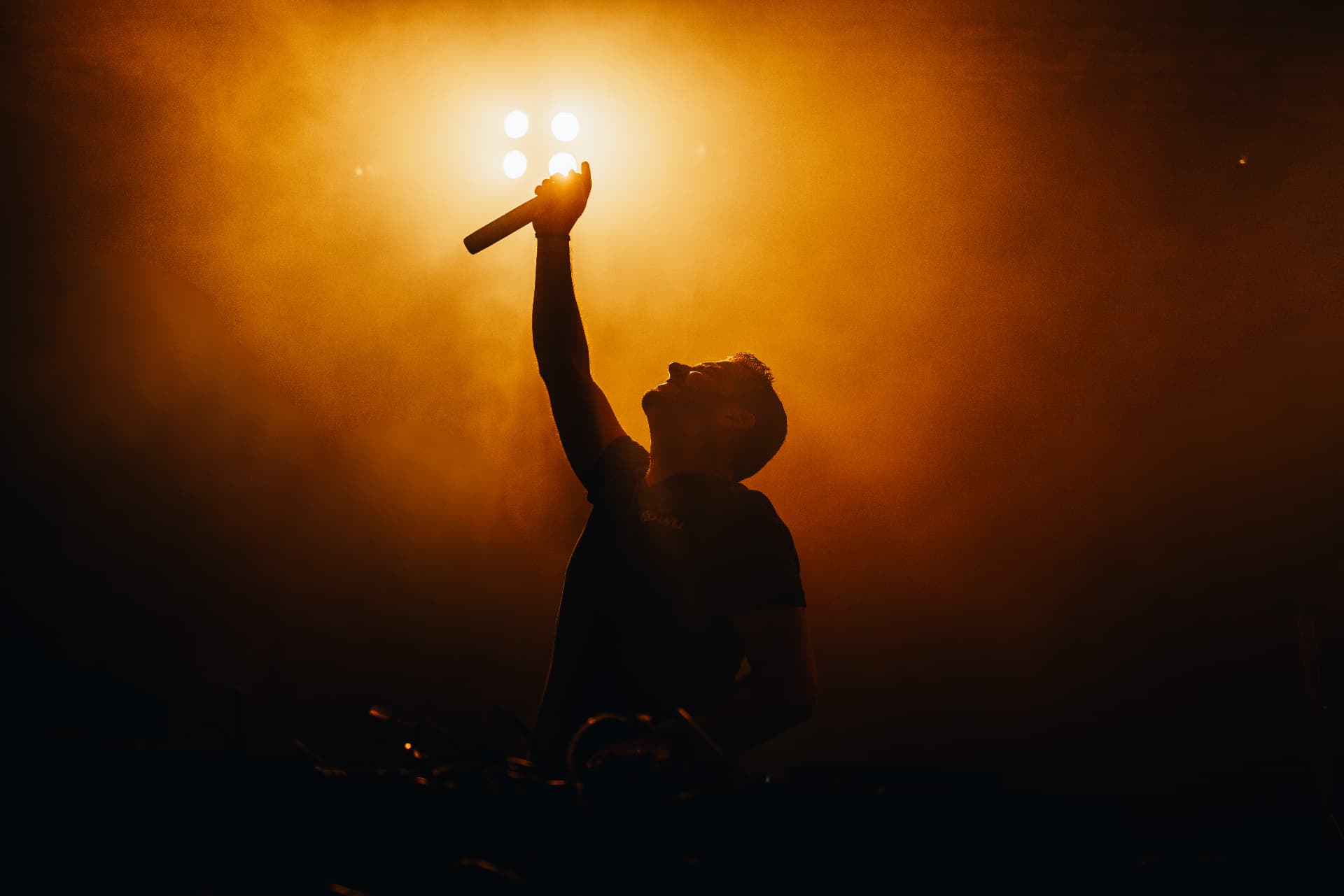Singer silhouetted against glowing stage lights with microphone raised, live concert performance shot by Paul Rumplmaier